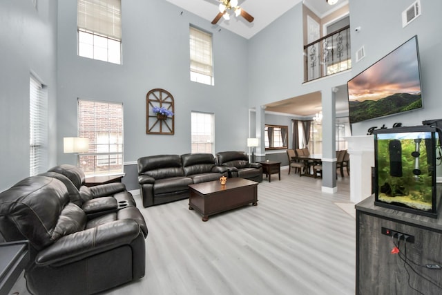 living room with ceiling fan, a towering ceiling, and light wood-type flooring