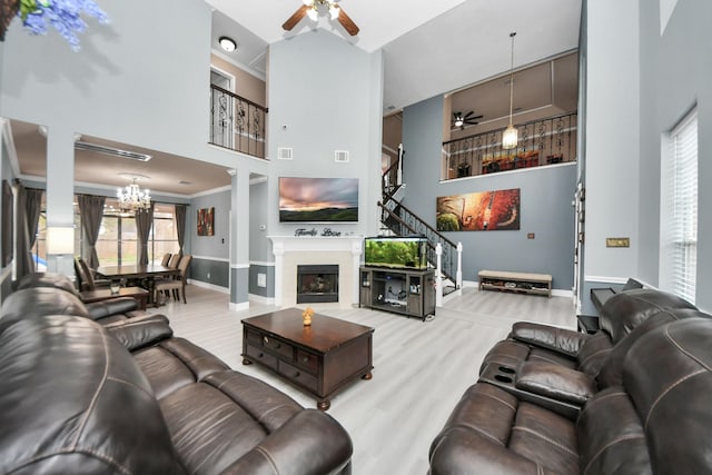 living room with crown molding, ceiling fan with notable chandelier, light hardwood / wood-style floors, and a high ceiling