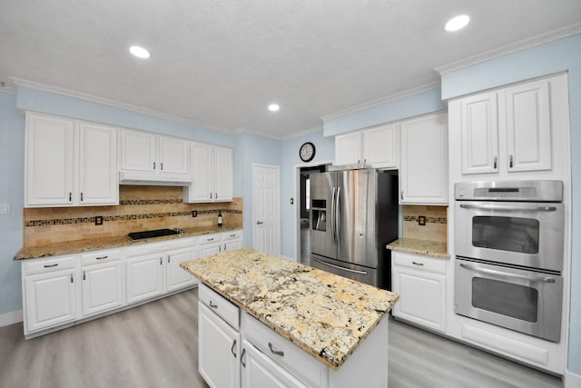 kitchen featuring appliances with stainless steel finishes, white cabinetry, a center island, ornamental molding, and light hardwood / wood-style floors