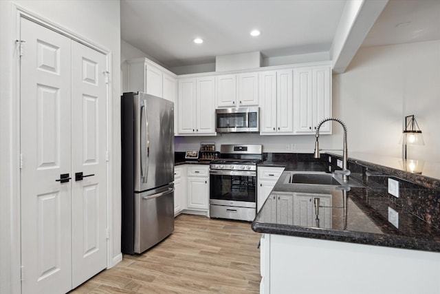 kitchen with kitchen peninsula, stainless steel appliances, white cabinets, dark stone counters, and sink