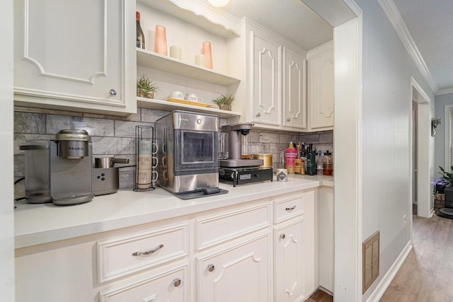 kitchen with light wood-type flooring, white cabinets, backsplash, and crown molding