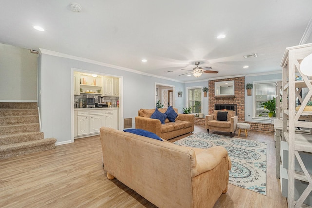 living room with a fireplace, ornamental molding, ceiling fan, and light wood-type flooring