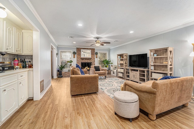 living room with a fireplace, ornamental molding, ceiling fan, and light wood-type flooring