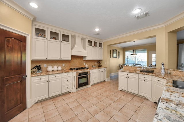 kitchen with stainless steel appliances, custom range hood, pendant lighting, white cabinets, and backsplash