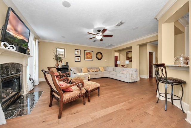 living room featuring a fireplace, ceiling fan, crown molding, and light hardwood / wood-style flooring