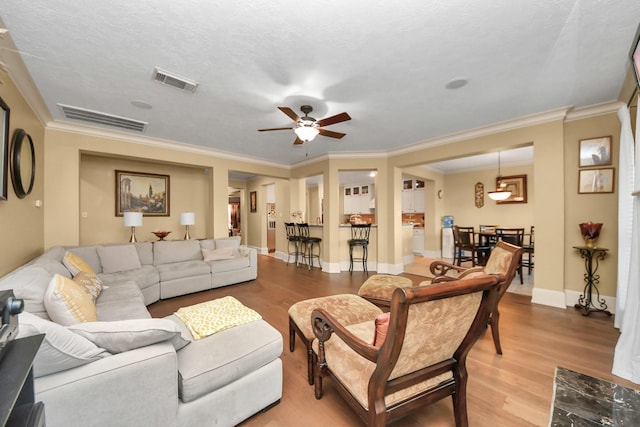 living room featuring light hardwood / wood-style floors, ceiling fan, crown molding, and a textured ceiling