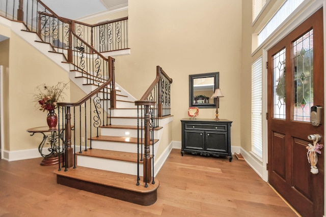 entrance foyer with light hardwood / wood-style floors, ornamental molding, and a towering ceiling