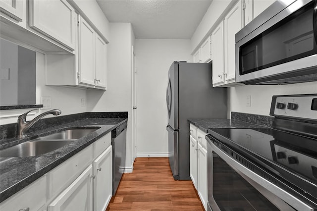 kitchen with dark stone countertops, wood-type flooring, sink, appliances with stainless steel finishes, and white cabinets