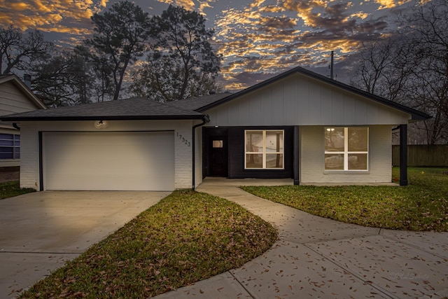 ranch-style house with roof with shingles, brick siding, a lawn, a garage, and driveway