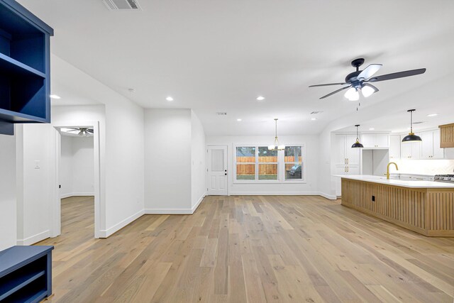 unfurnished living room with sink, ceiling fan with notable chandelier, and light hardwood / wood-style floors