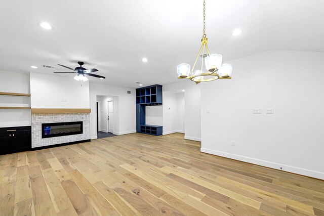 unfurnished living room with vaulted ceiling, a tiled fireplace, ceiling fan with notable chandelier, and light wood-type flooring