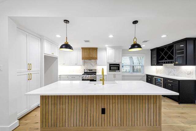 kitchen with appliances with stainless steel finishes, decorative light fixtures, and a kitchen island with sink