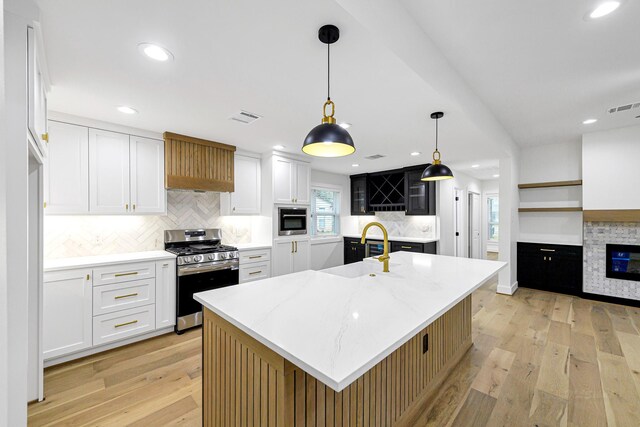 kitchen with white cabinetry, decorative light fixtures, a center island with sink, and stainless steel gas stove