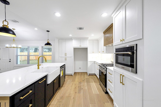 kitchen with stainless steel appliances, a center island with sink, white cabinets, and decorative light fixtures