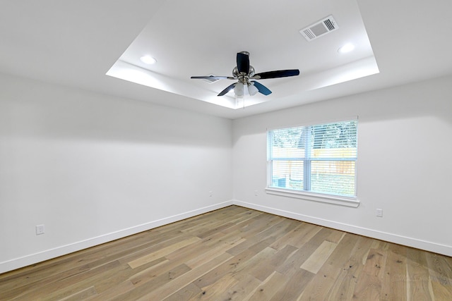 spare room featuring a tray ceiling, ceiling fan, and light wood-type flooring