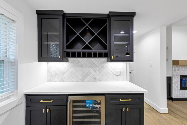 bar featuring wine cooler, light stone countertops, decorative backsplash, and light wood-type flooring