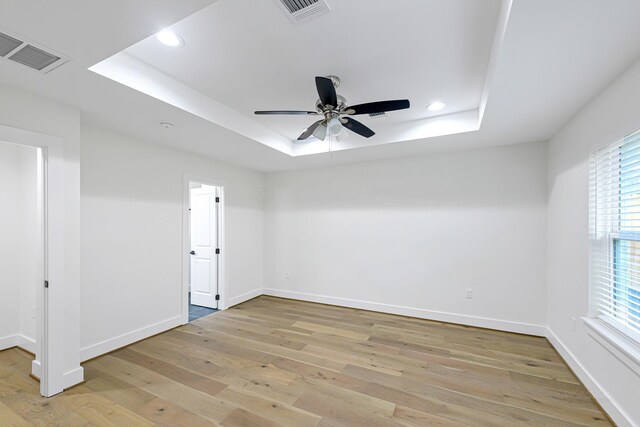 unfurnished room featuring a raised ceiling, ceiling fan, and light wood-type flooring