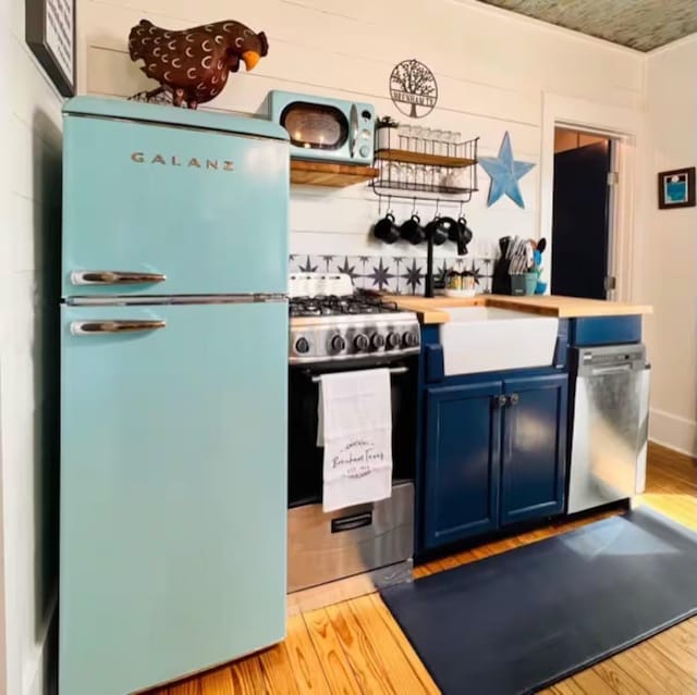 kitchen with wood walls, appliances with stainless steel finishes, blue cabinets, light hardwood / wood-style flooring, and sink