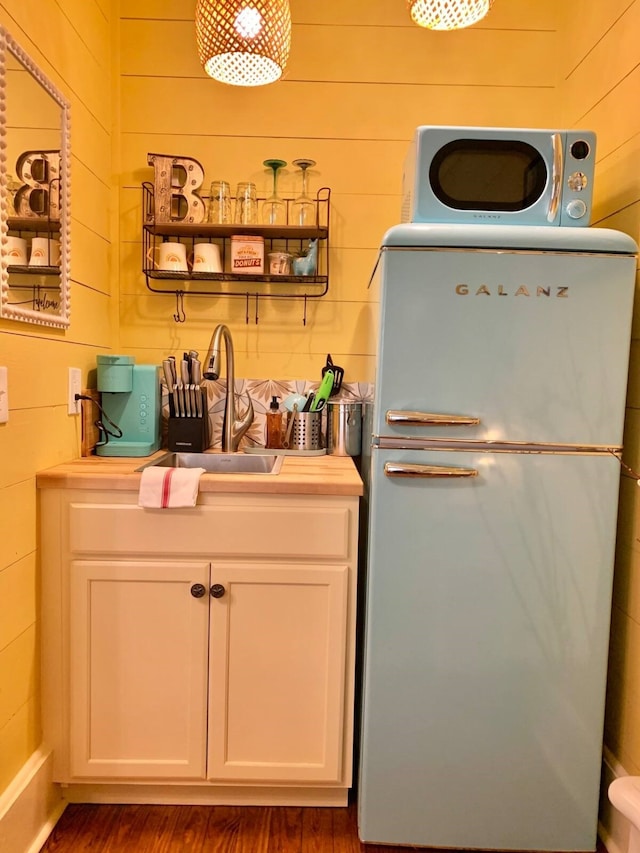 bar with fridge, white cabinets, sink, and wooden walls