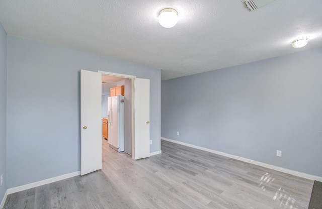 spare room with light wood-type flooring and a textured ceiling