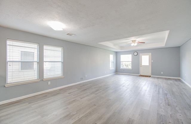 spare room with ceiling fan, light hardwood / wood-style flooring, a raised ceiling, and a textured ceiling