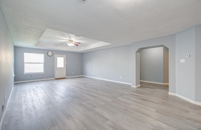 empty room featuring a textured ceiling, ceiling fan, a tray ceiling, and light hardwood / wood-style flooring