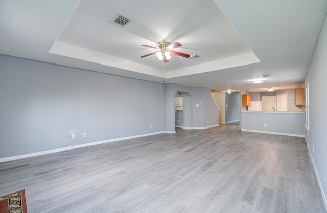 unfurnished living room featuring light wood-type flooring, ceiling fan, and a tray ceiling