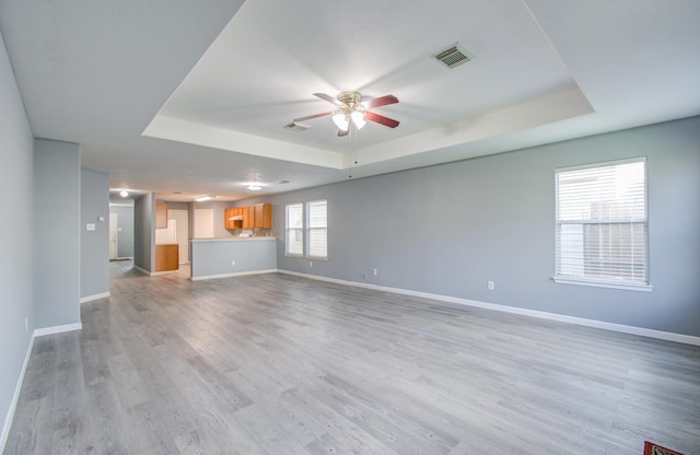 unfurnished living room with ceiling fan, light hardwood / wood-style flooring, and a tray ceiling