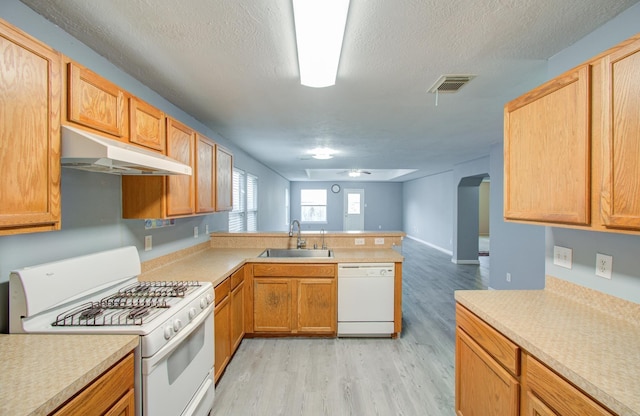 kitchen with white appliances, light wood-type flooring, kitchen peninsula, a textured ceiling, and sink