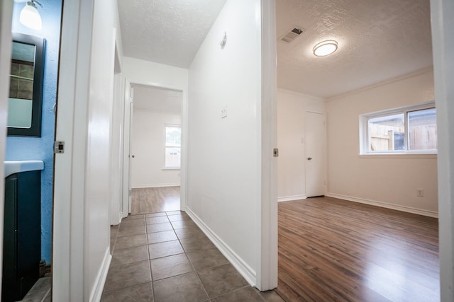 corridor with dark tile patterned floors, a textured ceiling, and crown molding