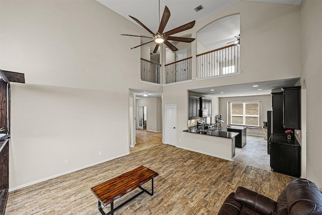 living room featuring ceiling fan, a towering ceiling, and hardwood / wood-style floors