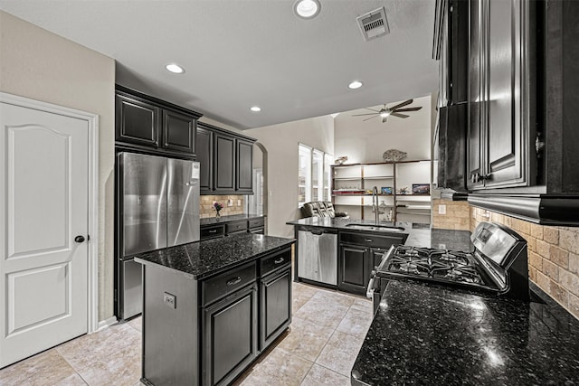 kitchen with a kitchen island, decorative backsplash, sink, appliances with stainless steel finishes, and dark stone counters