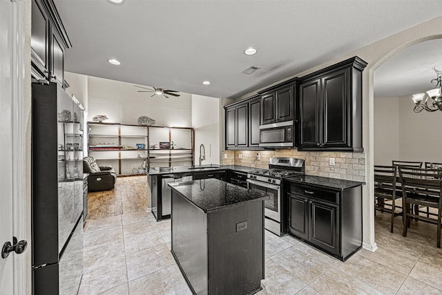 kitchen featuring ceiling fan with notable chandelier, a center island, stainless steel appliances, dark stone countertops, and sink