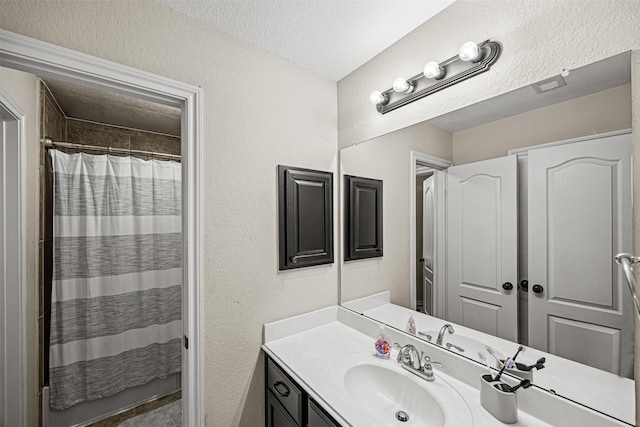 bathroom with a textured ceiling, walk in shower, and vanity