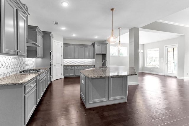 kitchen featuring sink, gray cabinets, an island with sink, decorative light fixtures, and dark stone counters