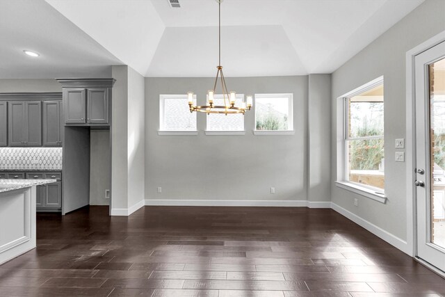 unfurnished dining area featuring dark hardwood / wood-style flooring, a notable chandelier, a tray ceiling, and lofted ceiling