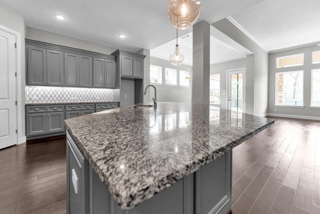 kitchen featuring gray cabinets, pendant lighting, sink, backsplash, and dark stone counters