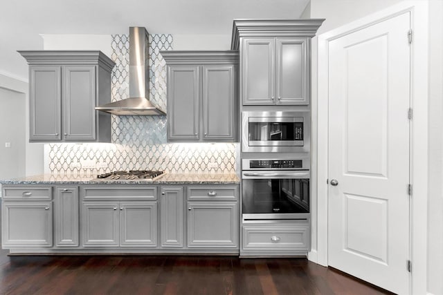 kitchen with wall chimney range hood, gray cabinetry, stainless steel appliances, tasteful backsplash, and light stone countertops