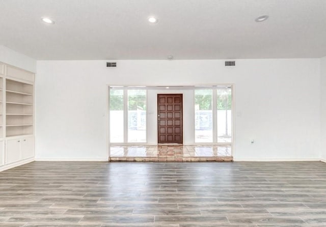 unfurnished living room featuring built in shelves and plenty of natural light