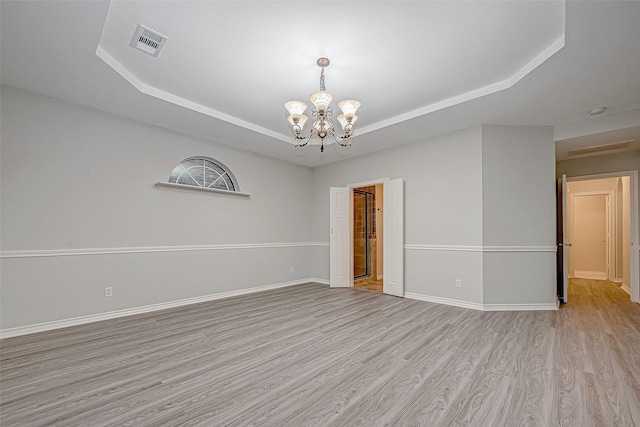 empty room featuring light wood-type flooring, an inviting chandelier, and a tray ceiling