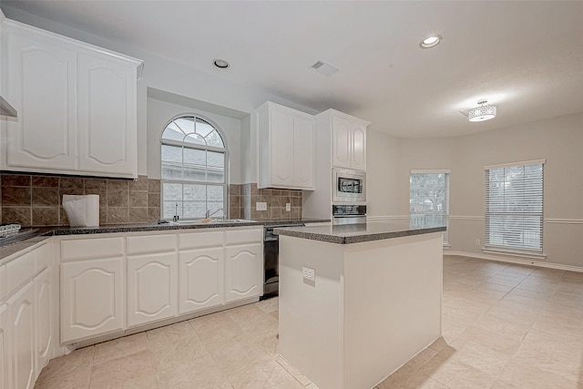 kitchen with white cabinetry, stainless steel microwave, black dishwasher, backsplash, and a kitchen island