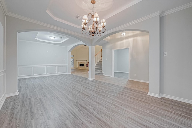 unfurnished living room with crown molding, a tray ceiling, light wood-type flooring, and an inviting chandelier