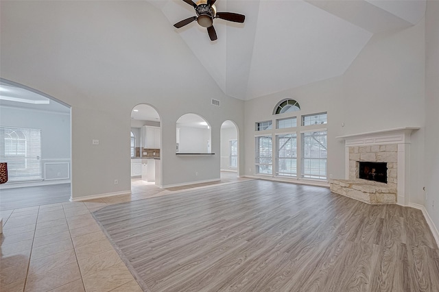 unfurnished living room with ceiling fan, a stone fireplace, light hardwood / wood-style floors, and high vaulted ceiling