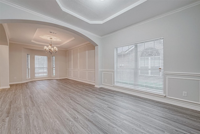 empty room with light hardwood / wood-style floors, a tray ceiling, a textured ceiling, a chandelier, and crown molding