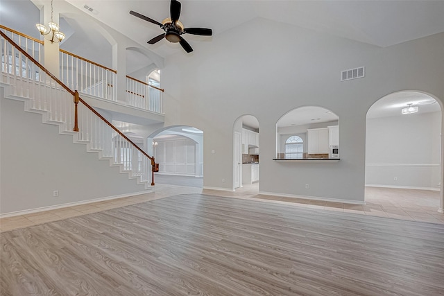 unfurnished living room featuring light wood-type flooring, ceiling fan with notable chandelier, and a towering ceiling