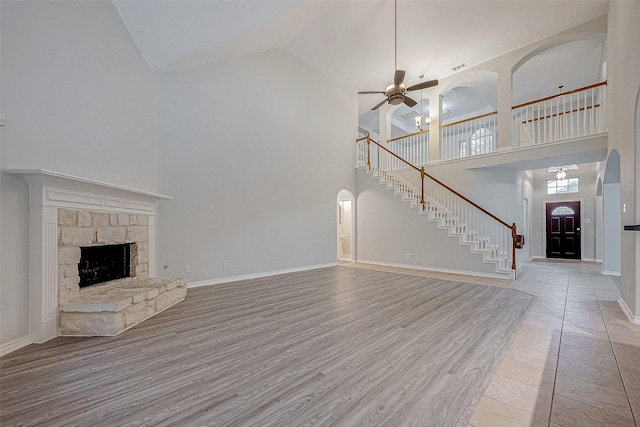 unfurnished living room featuring a fireplace, ceiling fan, light hardwood / wood-style floors, and a towering ceiling