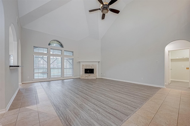 unfurnished living room with ceiling fan, light tile patterned floors, a towering ceiling, and a stone fireplace