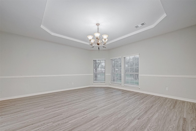 unfurnished room featuring a tray ceiling, an inviting chandelier, and light wood-type flooring