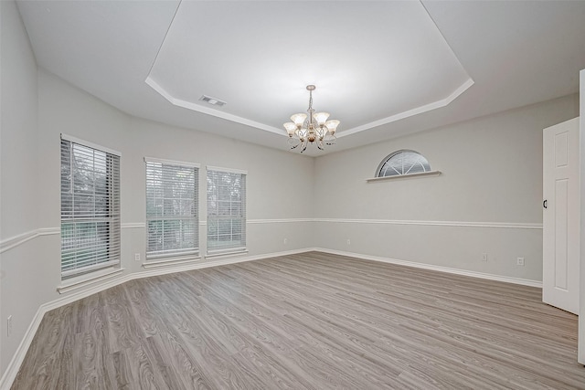 spare room featuring light wood-type flooring, an inviting chandelier, and a raised ceiling