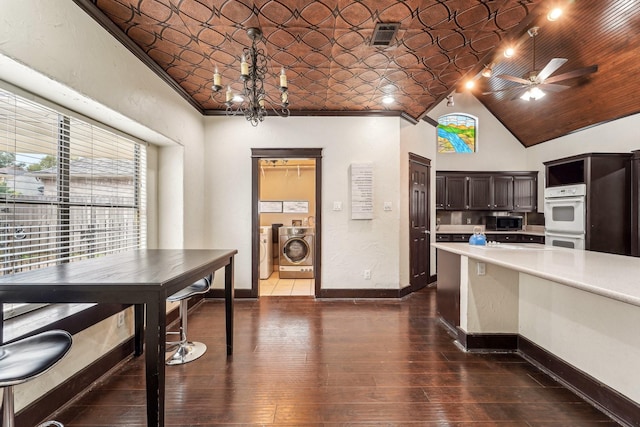 kitchen featuring washing machine and clothes dryer, white double oven, dark wood-type flooring, dark brown cabinets, and ceiling fan with notable chandelier